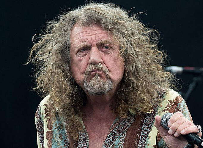 72 year old Led Zeppelin lead singer with loosely curled long hair, Robert Plant, pouts his lips while grabbing the microphone, featured in the Best Hair in Rock and Roll.