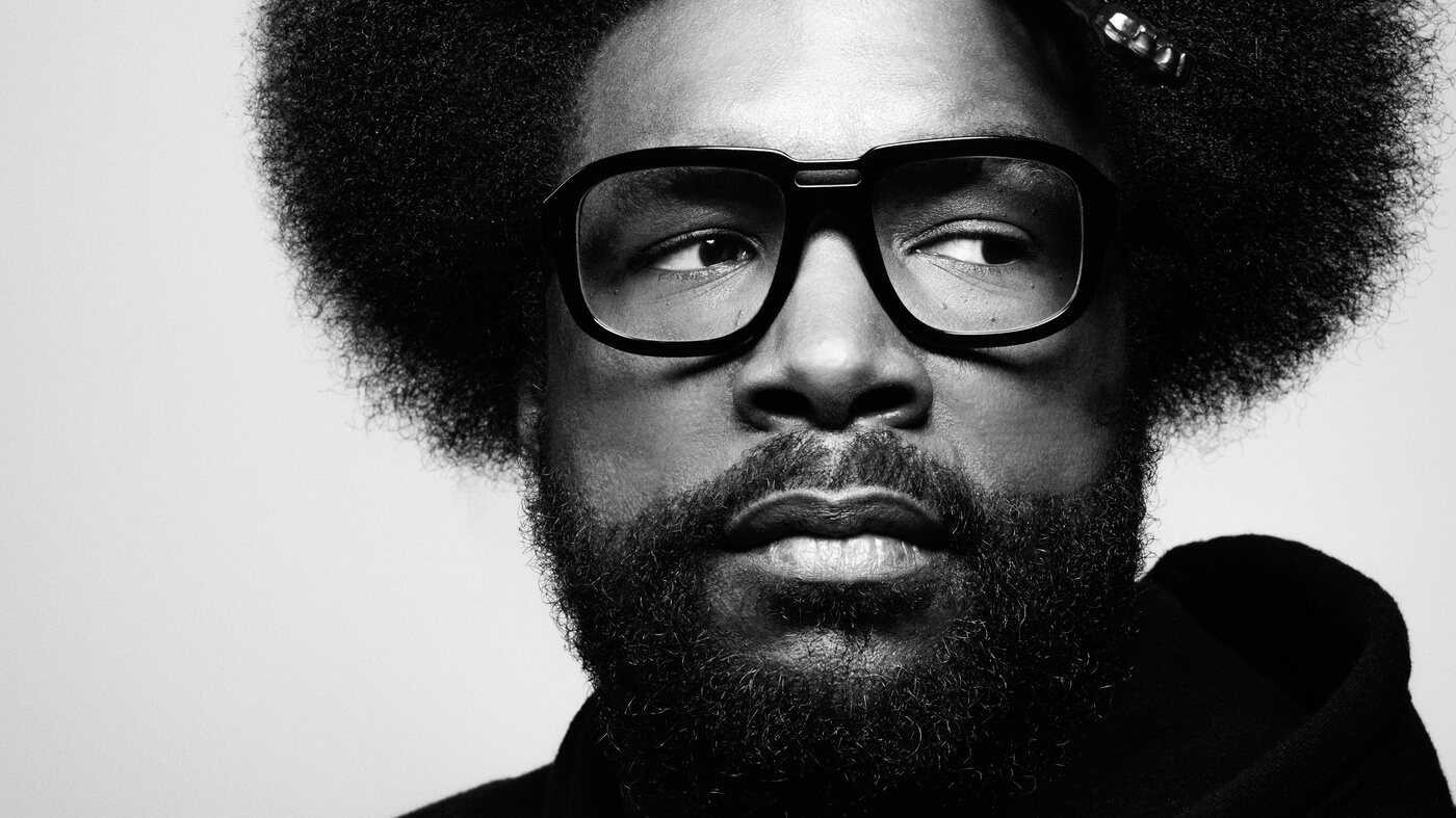 Questlove in a black and white photo, looking to the right through his glasses. His massive afro blows out of frame, but still, you can see his signature afro pickfeatured in the Best Hair in Rock and Roll.