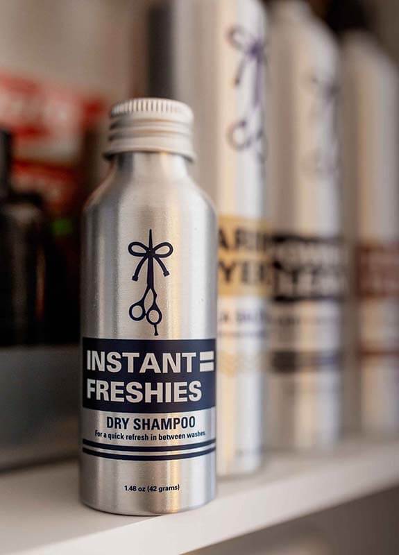 An aluminum bottle of INSTANT FRESHIES Dry Shampoo sitting in a medicine cabinet next to other products from The Longhairs.