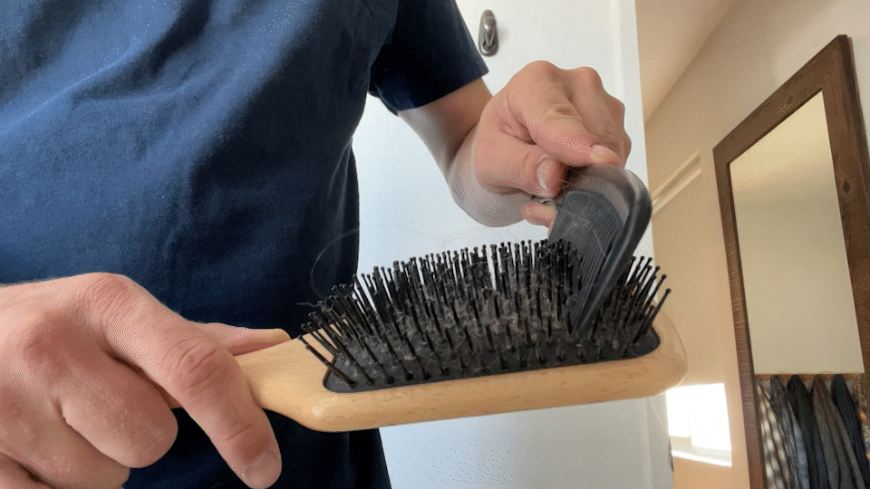Using a comb to brush and gather hair from The Continental paddle brush, featured in how to clean your hair brush