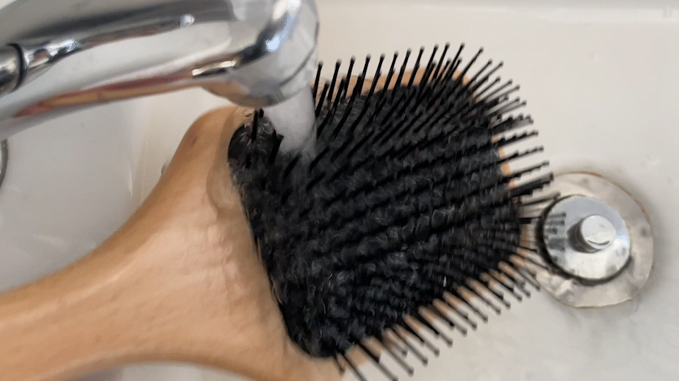 Running warm water over The Continental paddle brush, feature in how to clean your hair brush