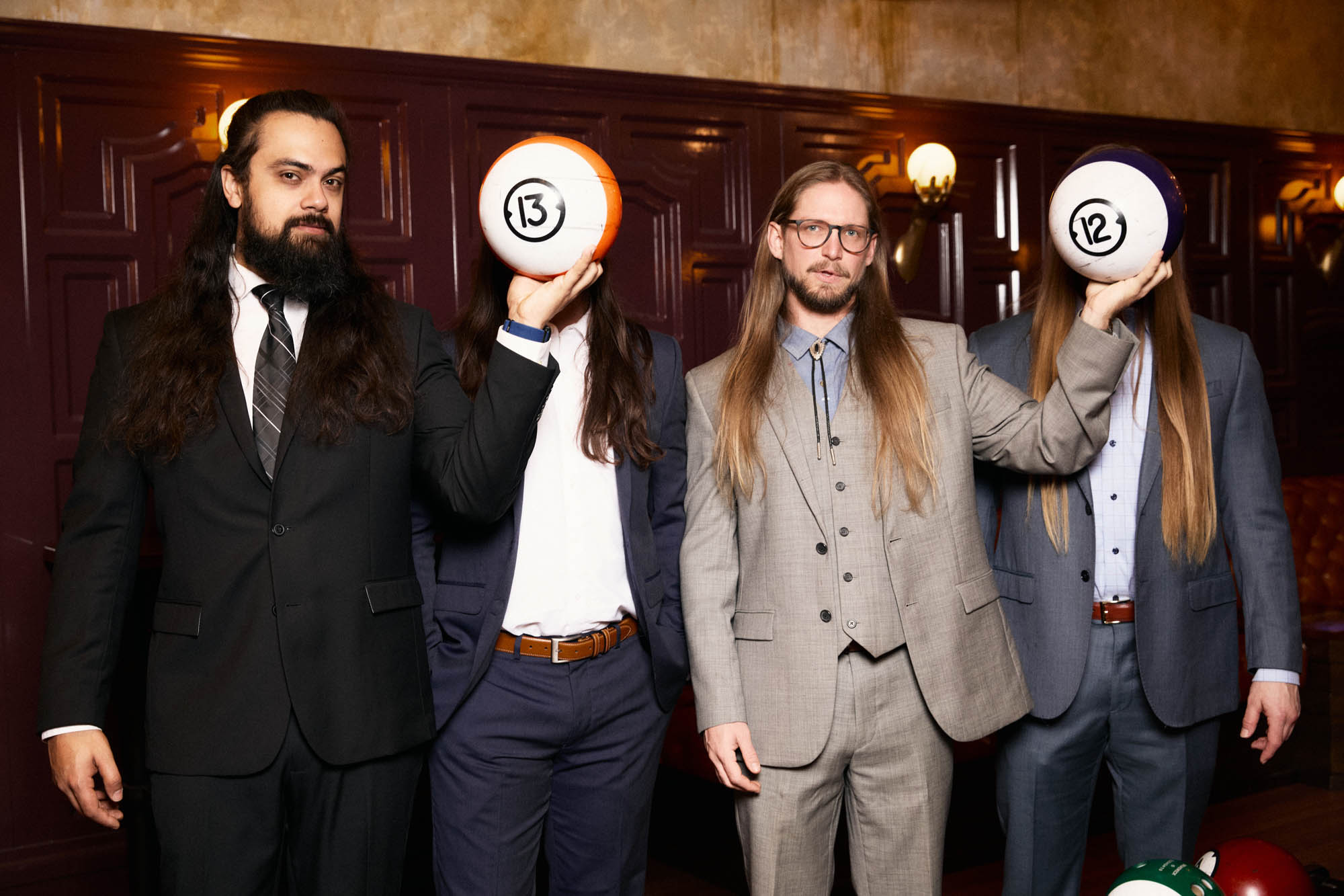 Jose Mejia, Chris Healy, Sean Horton, Lindsay Barto of The Longhairs, each wearing suits. Jose and Sean are holding bowling balls covering the faces of Linday and Chris. By Erica Joan 2024.