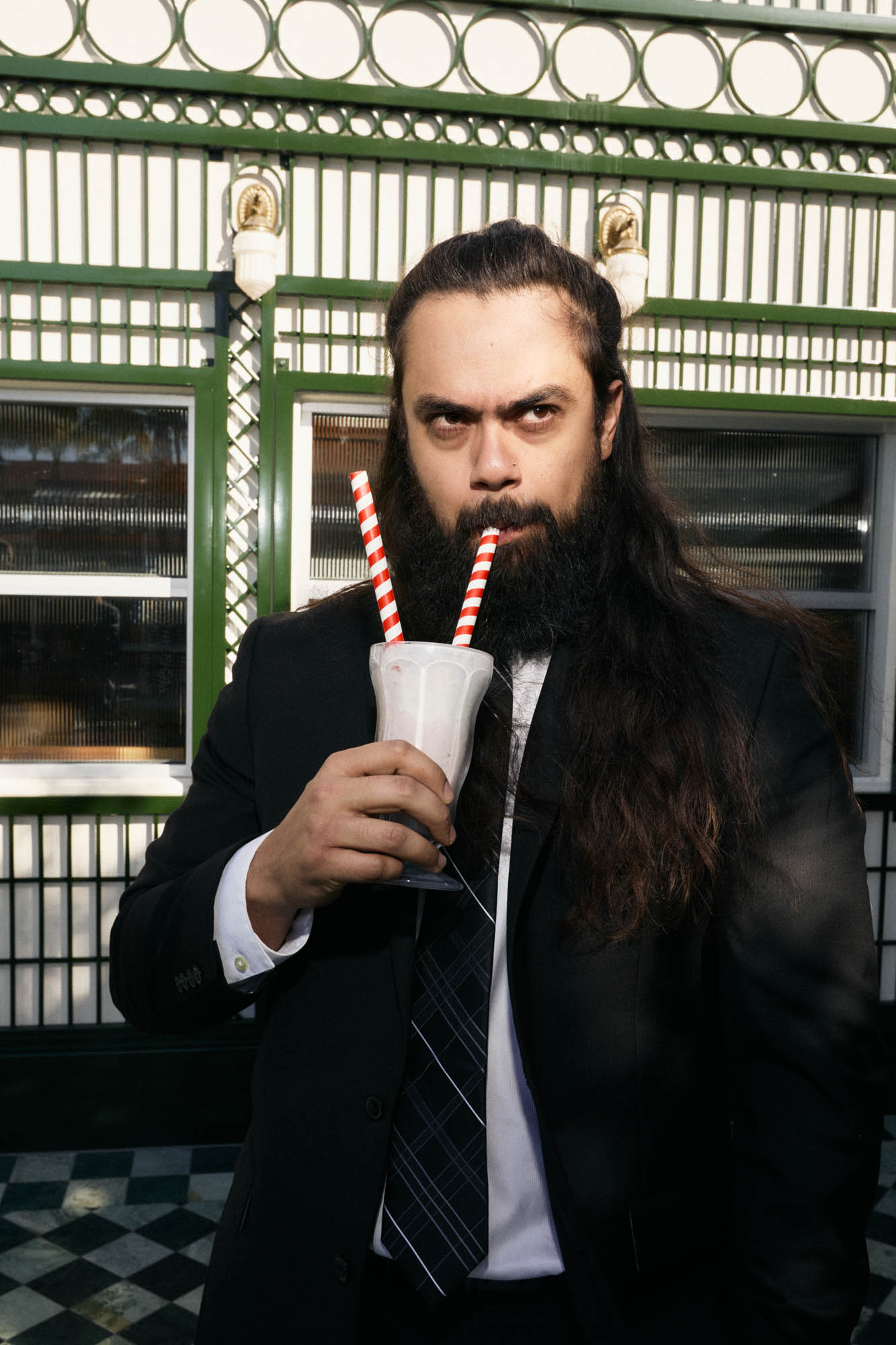 Jose Mejia of The Longhairs wearing a suit while enjoying a milkshake. By Erica Joan 2024.