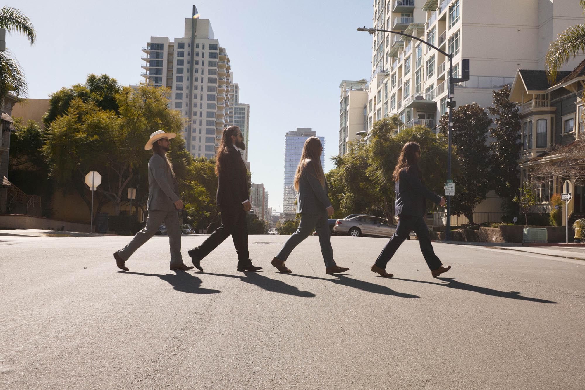 Sean Horton, Jose Mejia, Chris Healy and Lindsay Barto of The Longhairs, each wearing suits, walking across the street in classic form. By Erica Joan 2024.