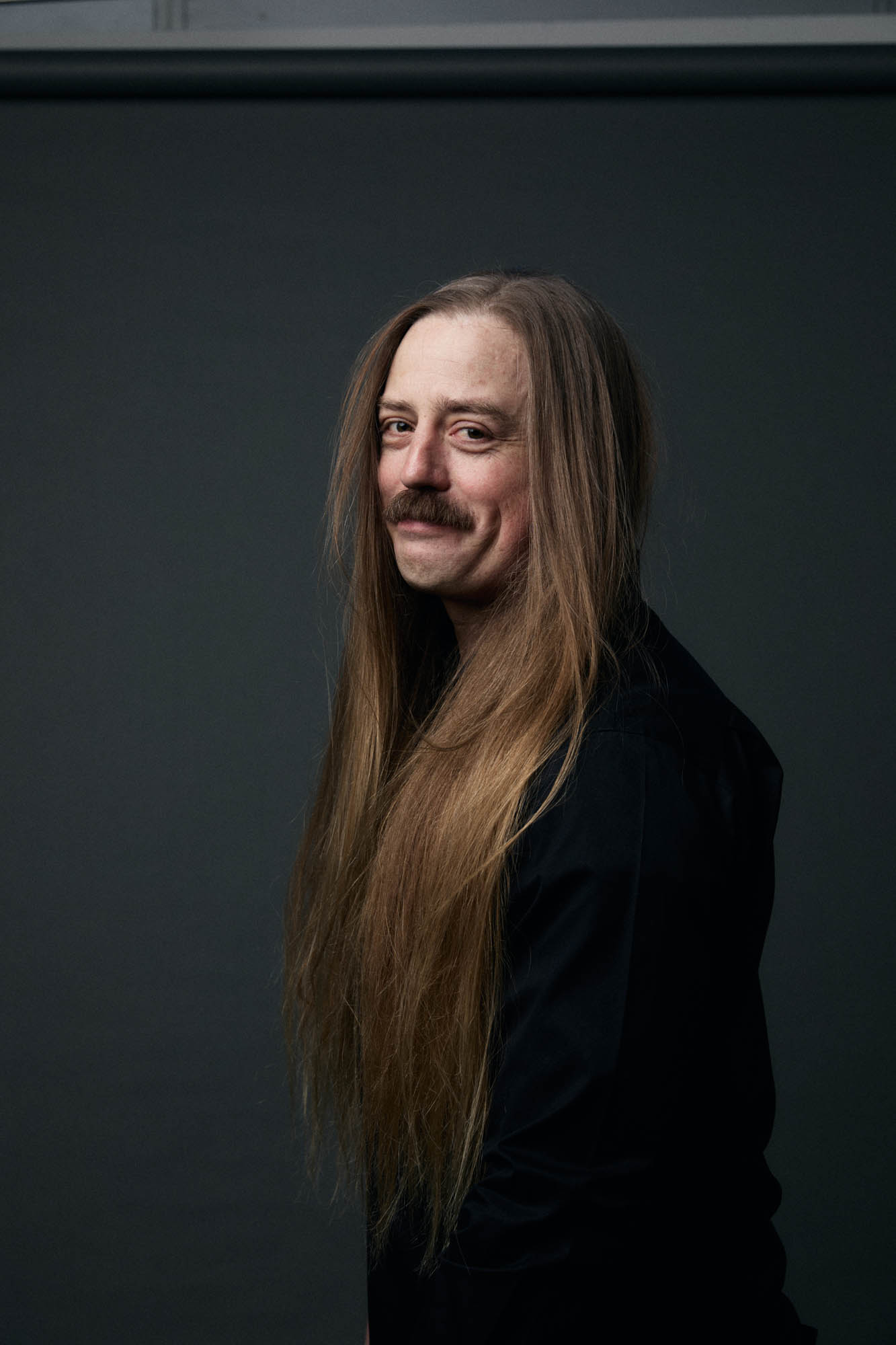 Chris Healy, CEO of The Longhairs, with a long, flowing, golden mane, smiling at the camera. By Erica Joan 2024.